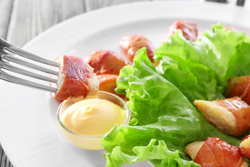 Dipping bacon wrapped chicken into gravy boat with sauce on plate