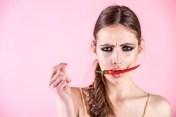 Woman hold red pepper in mouth on pink background