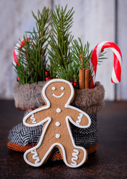 Christmas Holiday Card with Boots and Gingerbread Man Cookies. New Year Toy for Christmas Tree - shoes boots with fir branches, cany cane and cinnamon sticks on dark stone background. Copy space