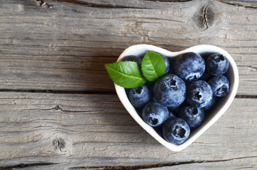 Fresh organic blueberries in a white heart shaped bowl on a burlap cloth on rustic wooden table.Blueberry.Bilberries.Healthy eating,vegan food,diet and nutrition concept.