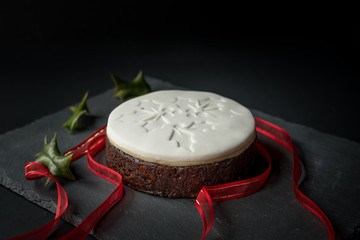 Christmas cake on dark background with holly and red ribbon