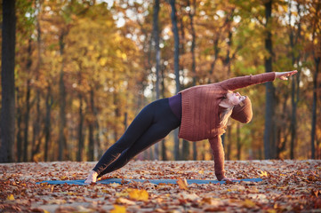 Beautiful young woman practices side bend yoga asana Vasishthasana on the wooden deck in the autumn park
