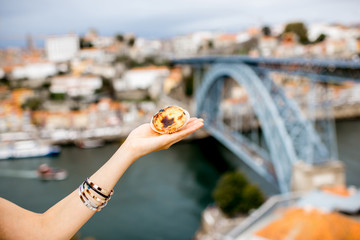 Holding traditional portuguese dessert called pastel de Nata on the beautiful cityscape background...