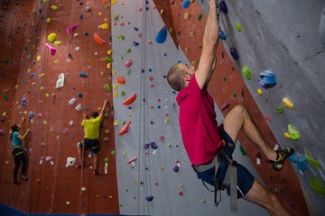 Confident athletes and trainer climbing wall in club