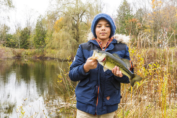 Young fisherman holding a bass he just caught on a fall day.