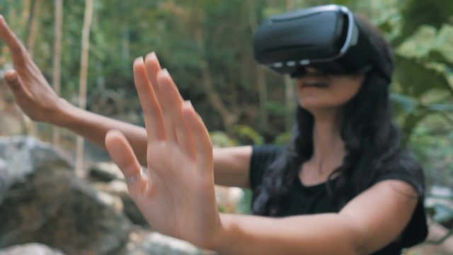 beautiful young brunette woman uses virtual reality glasses in the jungle