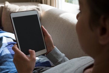 Woman using digital tablet on sofa in living room