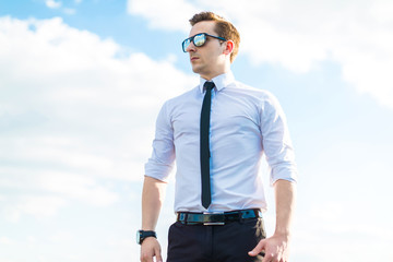 Attractive young busunessman in white shirt, tie and sunglasses stand on the roof