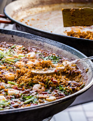 Paella dish with shrimp, closeup. Colorful Spanish paella rice in pan with vegetables and prawns. Empty pan in background.