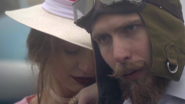 A woman in a white hat clings to a bearded pilot