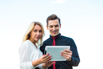 Couple of businessmen, good looking brunette man and attractive blonde woman stand on the roof and look in tablets