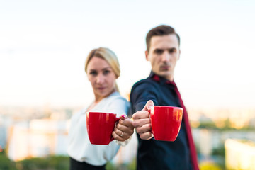 Couple of businessmen, attractive brunette man and pretty blonde woman stand on the roof and drink coffe