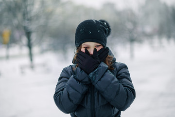 Fototapeta na wymiar girl covered mouth with gloves. The girl made a gesture, silence. A child walks after school on the street in a snowfall.