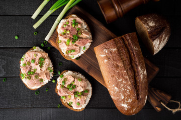 Open sandwiches with cottage cheese, canned tuna and green onions on black wooden background.