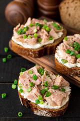 Open sandwiches with cottage cheese, canned tuna and green onions on black wooden background.