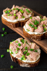 Open sandwiches with cottage cheese, canned tuna and green onions on black wooden background.