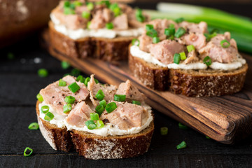 Open sandwiches with cottage cheese, canned tuna and green onions on black wooden background.