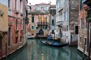 Fototapeta na wymiar The gondola with tourists sails in an old narrow Venetian canal