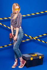 Attractive sexy builder girl in chechered shirt, jeans and glasses stand near the toolbox and hold...