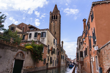 Fototapeta na wymiar Venetian narrow channel, bell tower and red clay tile roofs, view from the street