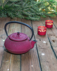 Red cast-iron Chinese teapot on a background of Christmas candles and a Christmas tree.