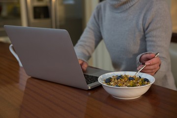 Mid section of woman having breakfast while using laptop