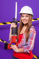 Sexy young builder girl in chechered shirt, helmet and jeans stand electro saw