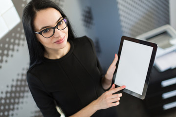Beautiful young businesswoman in black dress and glasses hold paper folder and show tablet