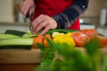 Mid section of woman cutting vegetable in kitchen