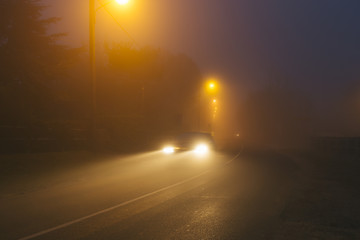 Country asphalt road in the region of Normandy, France in foggy day. Street lamps and car headlights at night. Toned
