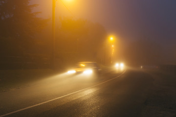 Country asphalt road in the region of Normandy, France in foggy day. Street lamps and car headlights at night. Toned
