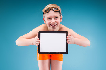 Teenage boy in orange shorts and swimming glasses hold empty tablet