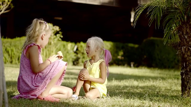 two cute children are sitting in a backyard on a green grass in shadows of trees in sunny summer day