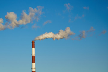 Smoky chimneys of a plant against a blue sky