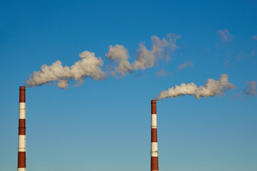 Smoky chimneys of a plant against a blue sky