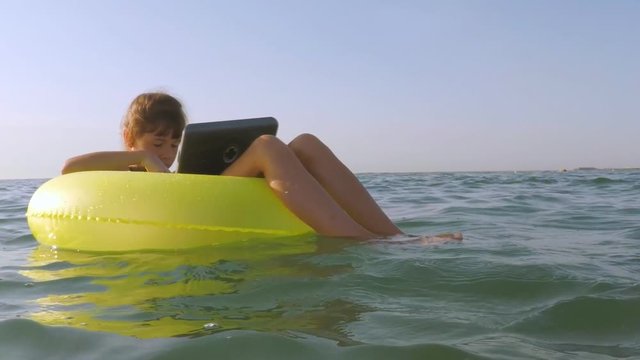 A child is floating in the water with a laptop. A little girl on an inflatable circle in the sea.