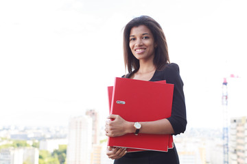 Fototapeta premium Attractive young businesslady in black strong suite hold red paper folders