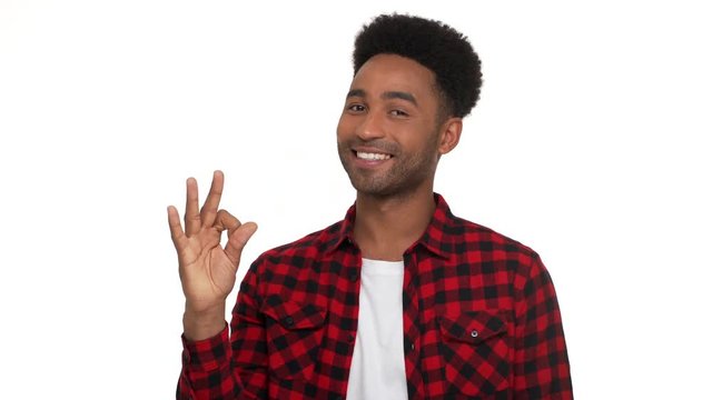 half-turn portrait of brunette afro guy wearing trendy red plaid shirt being satisfied showing OK sign meaning everything's fine isolated over white background. Concept of emotions