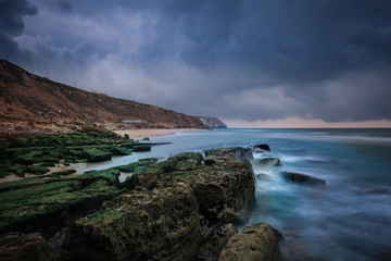 Fototapeta na wymiar Rocky beach seascape at sunrise. Long exposure from the rocky shore in the Portuguese coast
