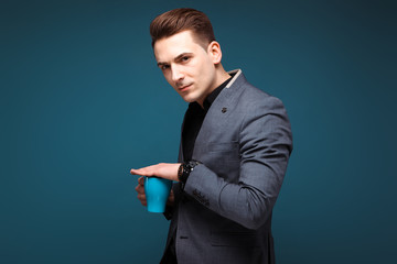 Young handsome businessman in grey jacket and black shirt hold blue cup