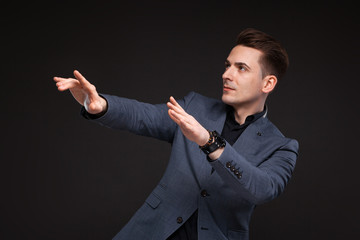 Young attractive businessman in grey jacket, costly watch and black shirt, black background