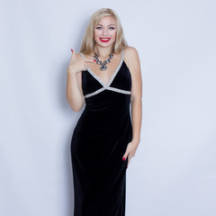 Beautiful blonde woman in black evening dress posing on grey background. Girl with black necklace