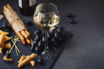 Cheese plate served with crackers, grapes and glass of white wine on dark background.