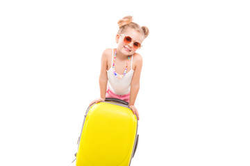 Cute young girl in white shirt, pink shorts and sunglasses stand near yellow suitcase