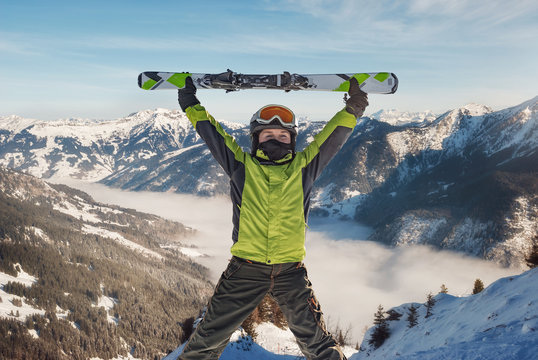 Happy young holding skis up in front of a mountain landscape