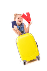 Pretty little girl in blue shirt, white shorts and sunglasses lean on the yellow suitcase and hold red cards and passport