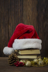 Obraz na płótnie Canvas Santa Claus hat, books, fir cone, viburnum, decorative boxes, balls and beads on a wooden background