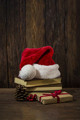 Obraz na płótnie Canvas A Santa Claus hat, books, boxes with a gift, a lump, a viburnum. Focus on the Santa Claus hat