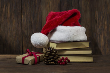 Obraz na płótnie Canvas Santa Claus hat, three books, boxes with a gift, a lump, a viburnum. Focus on the gift box