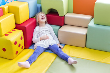 Little cute caucasian blond girl die laughing while playing with soft building blocks at indoor...